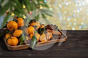 Christmas tangerines with leaves on a wooden tray with spices anise and cinnamon against the background of the New Year tree