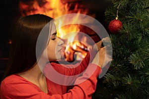Christmas theme. A young woman decorates a tree with toys on a fireplace background