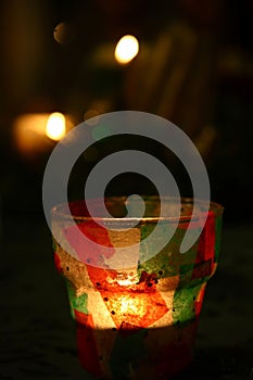 A Christmas themed candle holder with a lit candle, blurred Christmas lights in the background