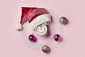 Christmas time.Christmas clock in a Santa Claus hat or cap on and christmas balls a pink background. The minute