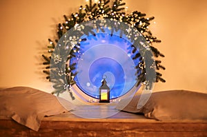 Christmas time. Vintage glowing lantern by round window decorated with tree branch and xmas lights photo