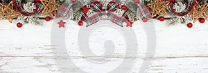 Christmas top border of ornaments, branches and red and green plaid bows and ribbon on a white wood background