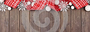 Christmas top border of red and white ribbon, baubles and snowflake decorations on a dark wood banner background