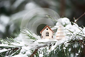 Christmas toy house with a toy tree on a natural natural background of a real fir in the snow, toned. Concept