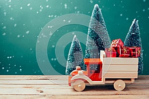 Christmas toy truck with gift boxes and pine tree on wooden table over green background