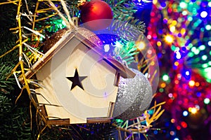 Christmas toy wooden house on the Christmas tree on the colorful lighting background. Beautiful Christmas decorations. Cool bright