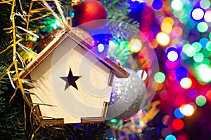 Christmas toy wooden house on the Christmas tree on the colorful lighting background. Beautiful Christmas decorations. Cool bright