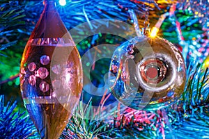 Christmas toys on the branches of decorative fir in the light of colorful lights of electric garland close-up