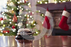 Christmas travel. Silver vintage bell on reception desk of guesthouse  and color shining garland on christmas tree on background