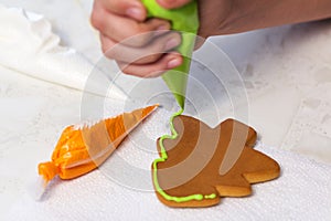 Baking holiday cookies. The child decorates homemade gingerbread in the form of a Christmas tree with green glaze.