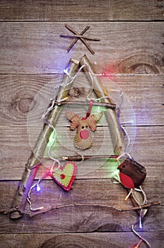 Christmas tree arranged from sticks, twigs, driftwood with glowing lights on wooden background. Handmade red and green