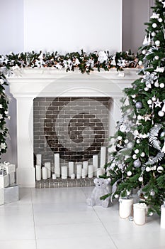 Christmas tree with balls, fireplace with candles and gifts in living room. Christmas interior of room is decorated in white color