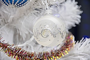 Christmas tree balls hang on the white artificial Christmas tree, holiday decorations.