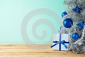 Christmas tree with blue ornaments and gift box on wooden table. Background for product montage display