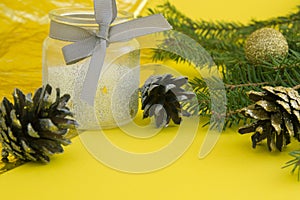 Christmas tree branch with cones and jar with candle on yellow background. happy new year 2021. merry christmas.