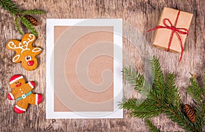 Christmas tree branch and gingerbread cookies on an old wooden background. Christmas decorations and blank sheet.