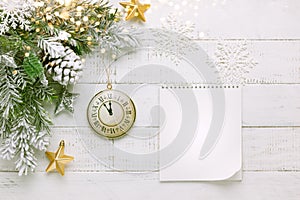 Christmas tree branch with pine cone in snow, retro style clock and notepad on a white wooden background. Winter or Christmas