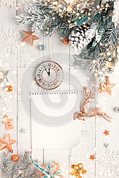 Christmas tree branch with pine cone in snow, retro style clock and notepad on a white wooden background. Winter or Christmas