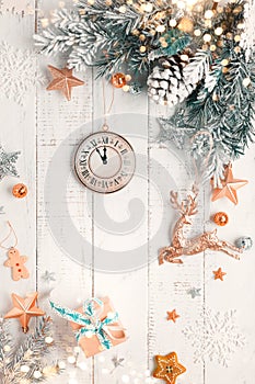 Christmas tree branch with pine cone in snow and retro style clock on a white wooden background. Winter or Christmas festive