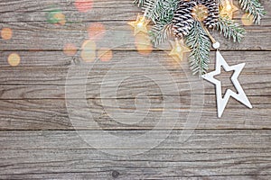 Christmas tree branch with pine cones decorated with star lights and wooden star on grey wooden  planks