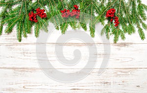 Christmas tree branch with red berries on wooden background.