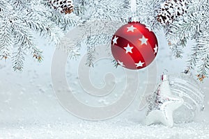 Christmas tree branch under white snow decorated with red ball and silver glass star