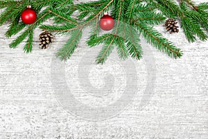 Christmas tree branches with balls and cones on the white wooden background.