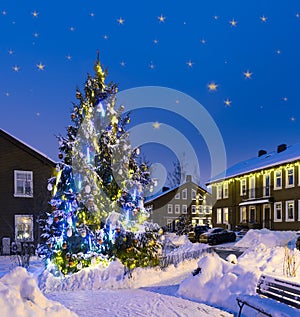 Christmas tree with bright lights on the street near the houses decorated for Christmas and New Year Eve at night