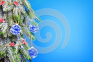 A Christmas tree covered with frost is decorated with paper balls and flags on a blue background. Christmas background