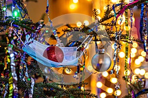 Christmas tree decorated with a medical mask with christmas ball in it, defocused lights on the background