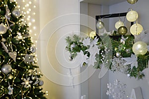 Christmas tree decorated with shiny garland and bulbs in white room. Festive vibes of winter holidays, Christmas details in