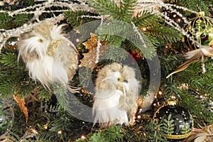 Christmas tree decorations. White glass owl, golden Christmas bauble, white feathers and lights in a pine tree. Close up