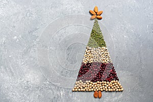 Christmas tree of different beans, chickpeas and almonds on a gray rustic background. The concept of holiday and vegetarian food.