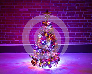 Christmas tree with festive lights in snow outdoors, purple brick wall background