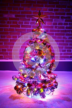 Christmas tree with festive lights in snow outdoors, purple brick wall background