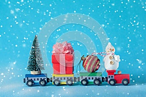 Christmas tree and gift box, ball and snowman on toy train on blue background. Gifts and congratulations concept