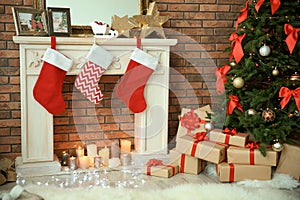 Christmas tree and gifts near decorative fireplace with stockings indoors