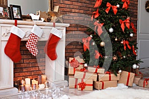 Christmas tree and gifts near decorative fireplace with stockings indoors