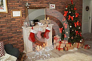 Christmas tree and gifts near decorative fireplace with stockings indoors