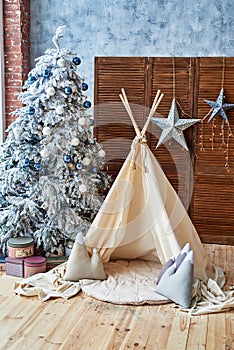 Christmas tree with gifts and wigwam in child room, copy space. Christmas decorations. Childen room interior with decorated play.