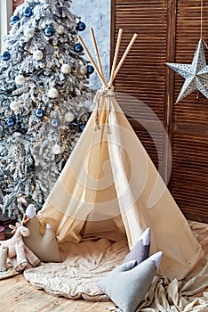 Christmas tree with gifts and wigwam in child room, copy space. Christmas decorations. Childen room interior with decorated play.