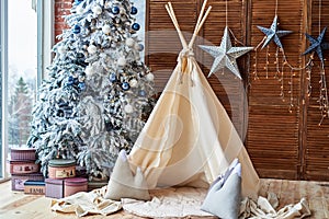 Christmas tree with gifts and wigwam near window in child room, copy space. Christmas decorations. Childen room interior.