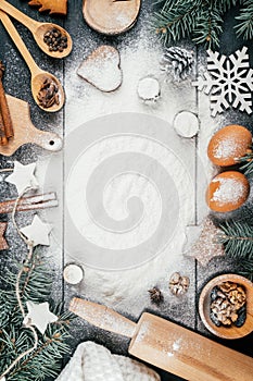 Christmas tree, gingerbread cookies, baking accessories and ingredients on black table with flour. Copy space. Vertical