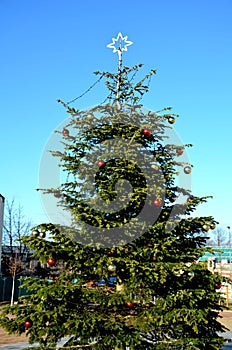 Christmas tree with glass decorations. sparsely decorated with a tip on which is an ice star from a light tube. blue spring sky, s