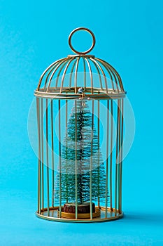 Christmas tree in a golden cage on a blue background, concept, surrealism. Fear of Christmas.