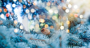 Christmas tree and lights bokeh around. New Year holidays concept with fir branches and pine cone on light background