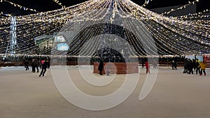 Christmas tree with lights on Ice Rink. People skating on an open air ice skating rink. Winter outdoor activities.