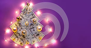 Christmas tree made of 100 dollar bills on purple background with copyspace and House key. Christmas decor of finance, savings,