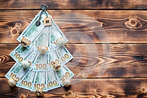 Christmas tree made of 100 dollar bills on wooden background with copyspace and House key. Christmas decor of finance, savings,