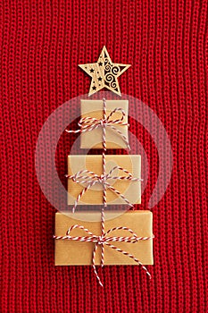 Christmas tree made of gift boxes and wooden star on red knitted background